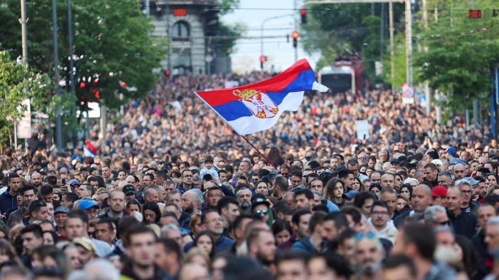 Протестующий размахивает сербским флагом над толпой в Белграде