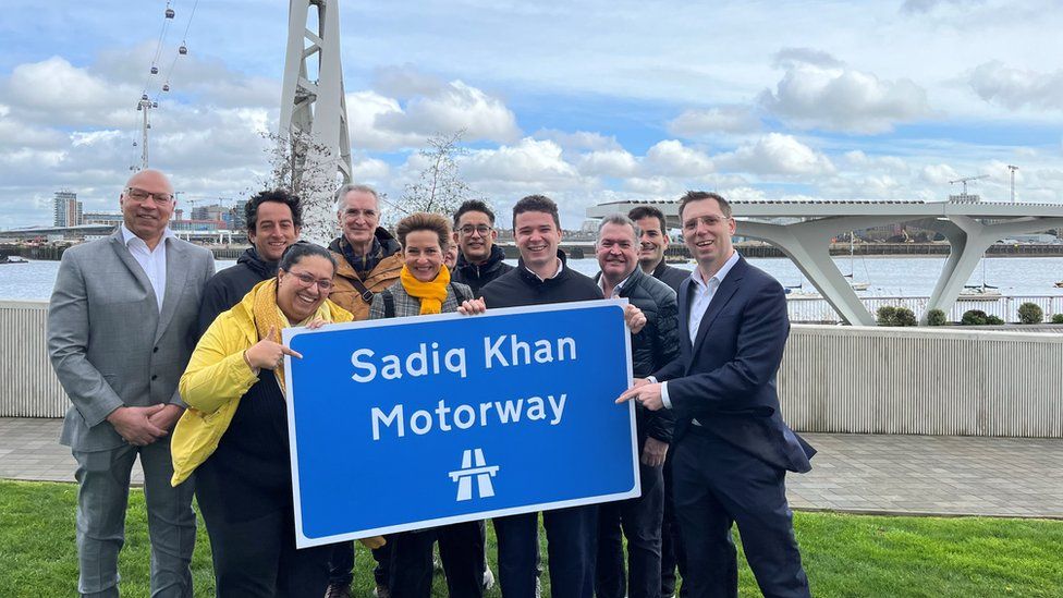 Image of Lib Dem Mayoral candidate with campaigners and a sign saying 'Sadiq Khan motorway'