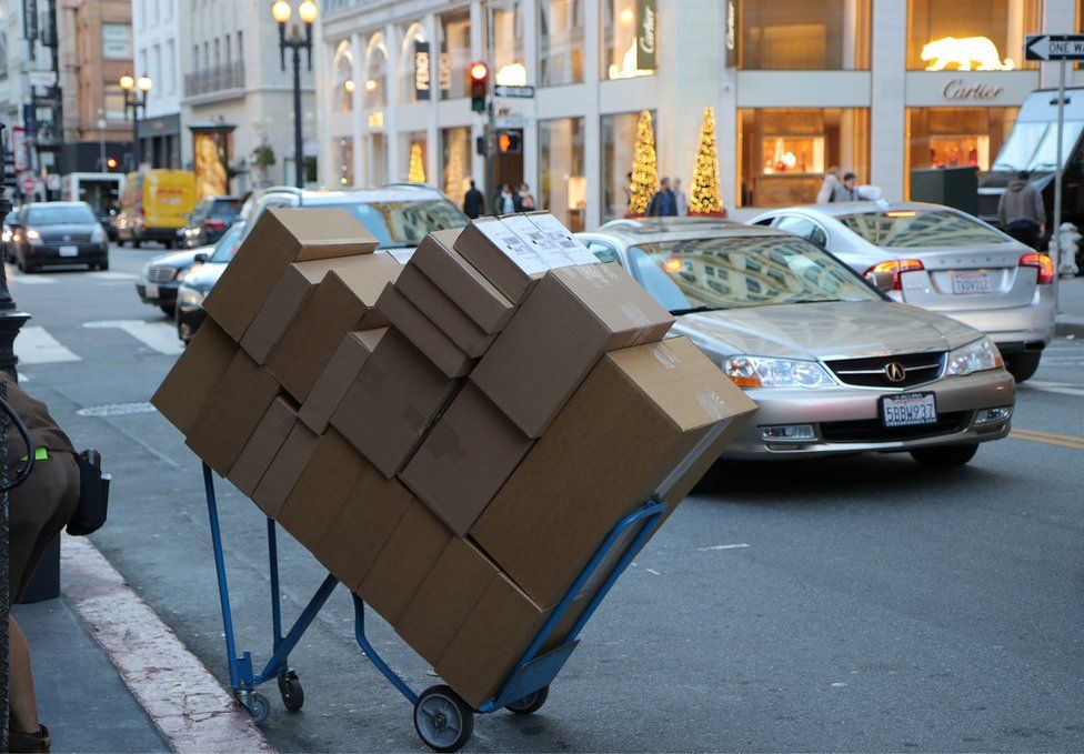A large pile of boxes neatly stacked on a trolley on a busy street