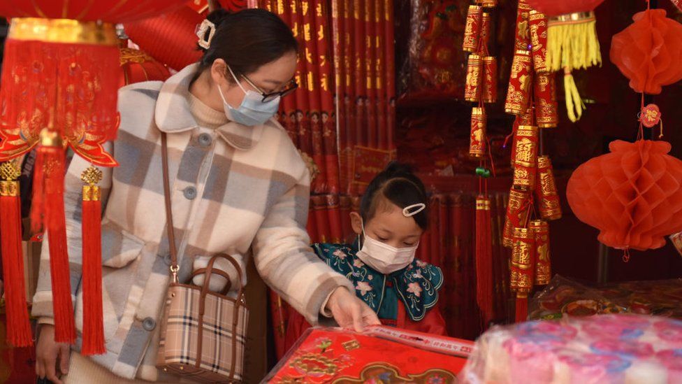 Mother and child wearing face masks buy New Year ornaments at sanliwan market in Fuyang City.