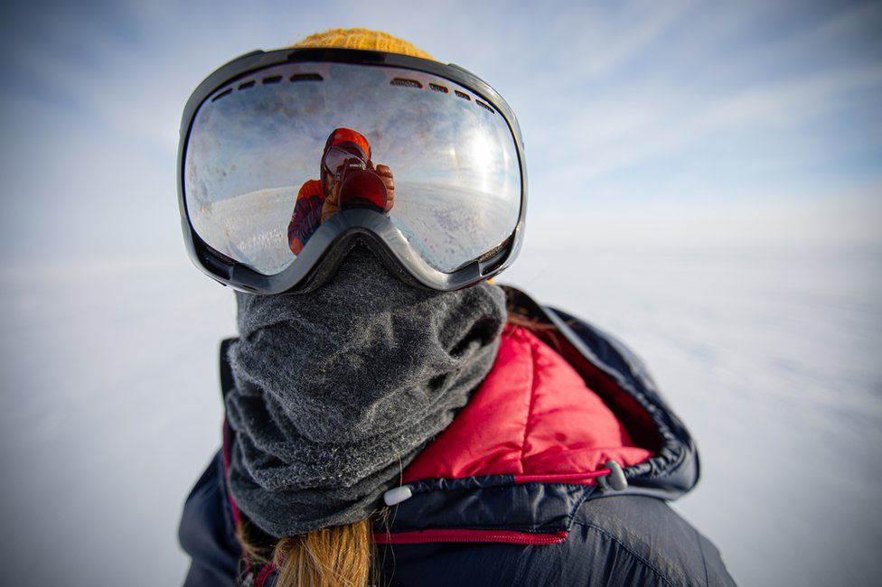 Person wearing a large pair of goggles - in icy Antarctic landscape... also a warm coat and scarf