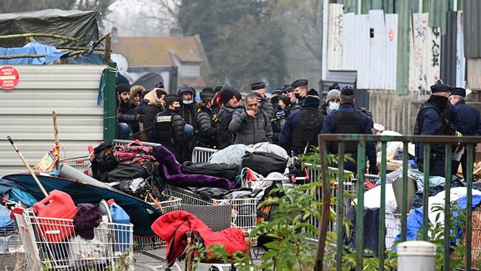 Migrants are escorted away from a migrant camp in northern France