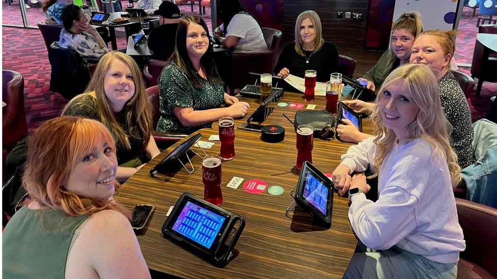 Becki Tate and six friends around a table playing bingo on tablet devices