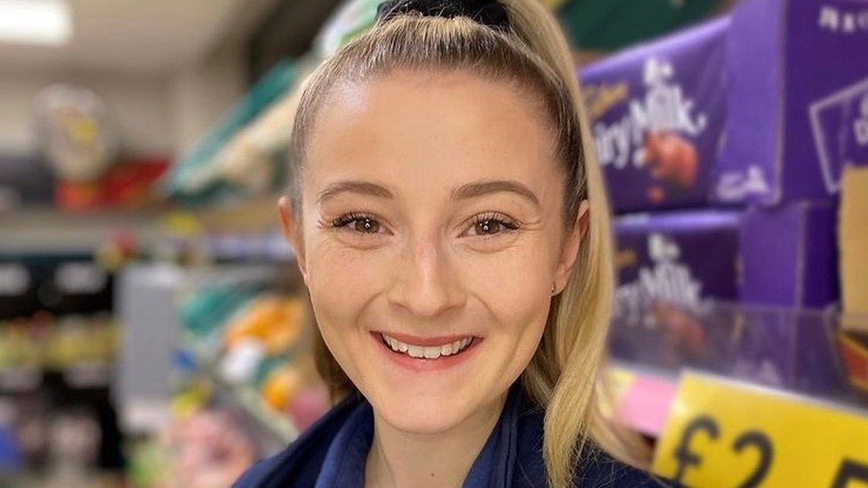Smiling lady with blonde pony tail with dairy milk on supermarket shelves in background