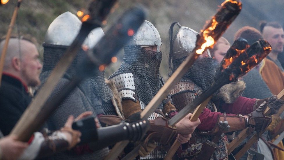 Viking re-enactment featuring multiple fighters in armour, some with burning sticks