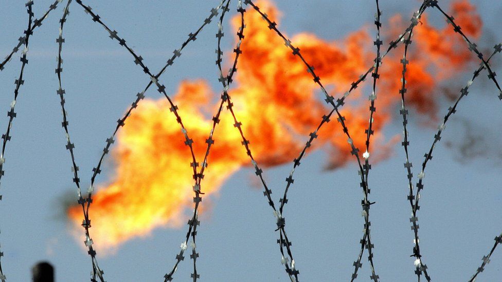 A gas flame is seen behind a barbed wire in the former Yukos and current Rosneft oil company production plant in Prirazlomnoye, western Siberia