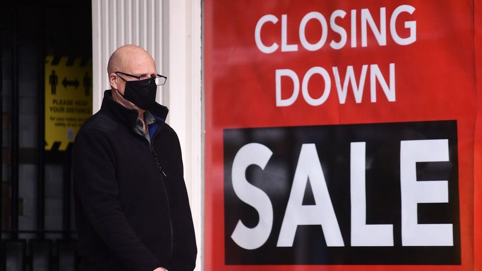 Masked man walking in front of shop closure sign