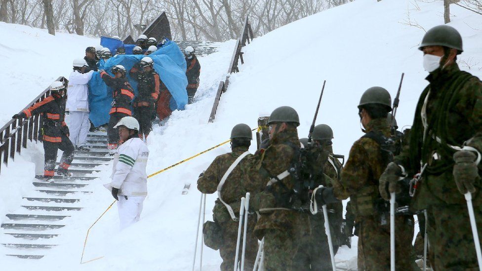 Пожарные несут выжившего, которого они спасли с места схода лавины в городе Насу, префектура Тотиги, 27 марта 2017 года, в то время как Самооборона Персонал Force смотрит на