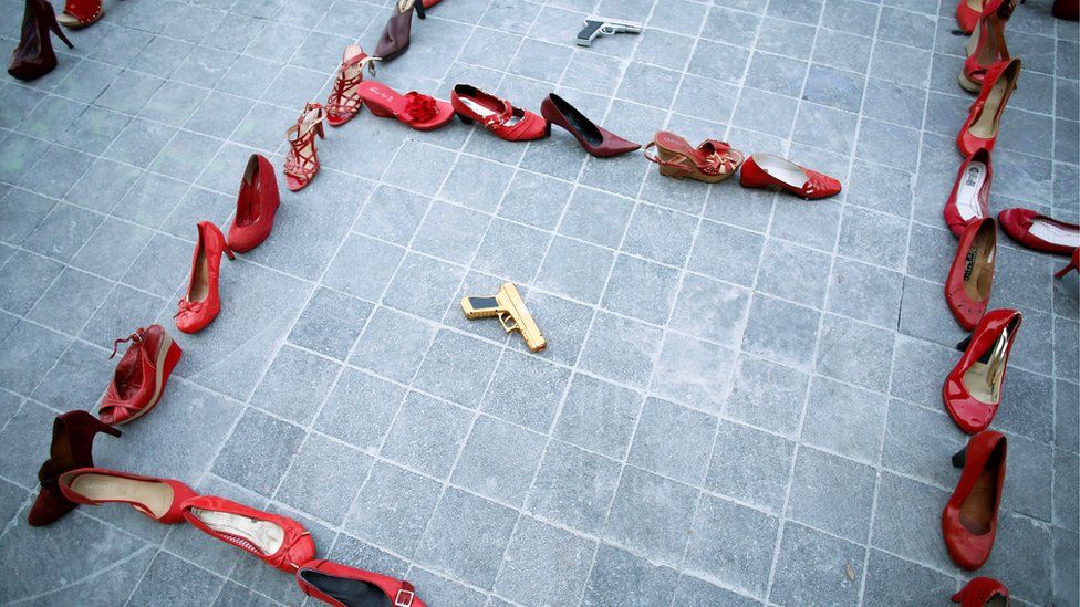 Pairs of women's red shoes are displayed next to a toy gun during the "Day without women" protest