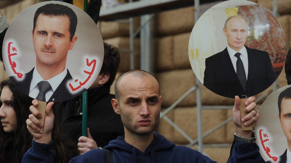 A pro-regime supporter holds photos of President Assad and President Putin