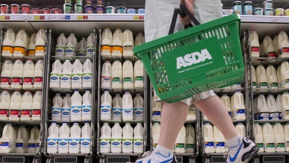 A shopper walks past milk cartons in an aisle of Asda