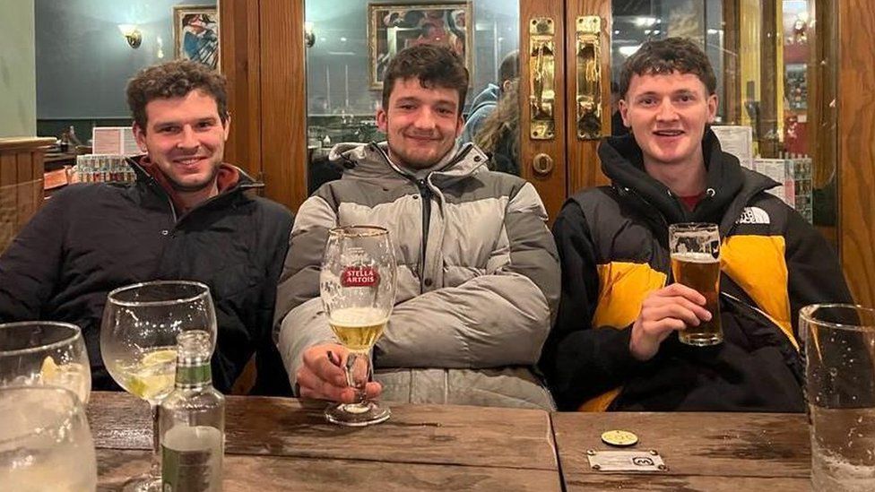 Three men in the pub smiling to camera