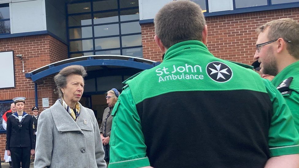 Princess Anne in front of the Devizes building listening to two people from St John Ambulance wearing green uniforms