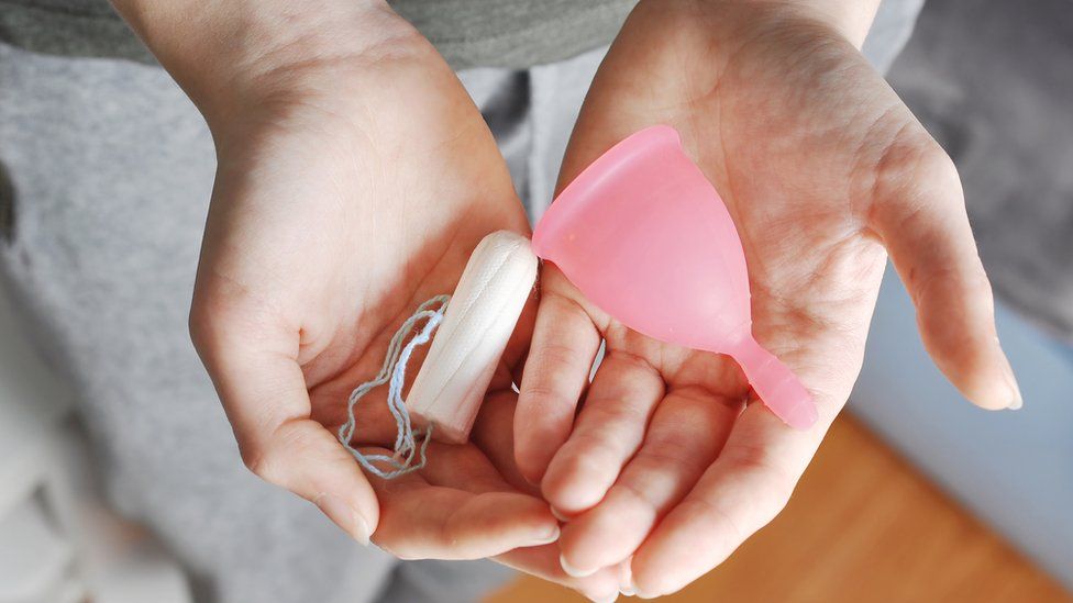 Woman holding a menstrual cup and a tampon