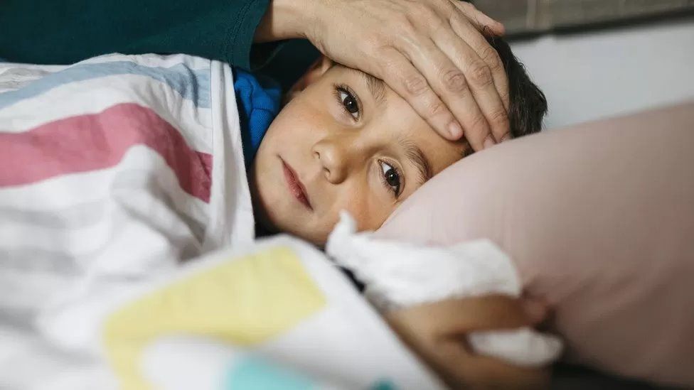 Stock image of a boy lying in bed having his temperature checked