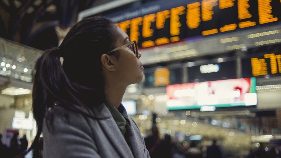 Женщина смотрит на табло отправления поезда
