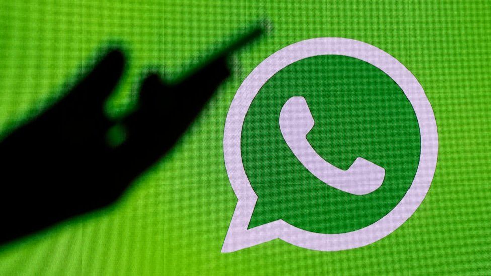 silhouette of hand holding phone next to WhatsApp logo