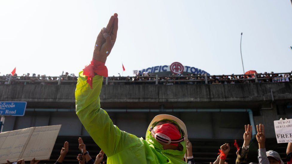 A protester wearing a mask makes a three-finger salute