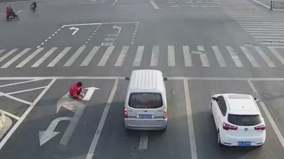 A Chinese man paints his own traffic signs while cars continue on their way