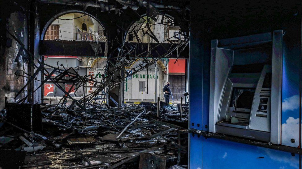 People inspect a fire-damaged bank in the Lebanese city of Tripoli on 28 April 2020