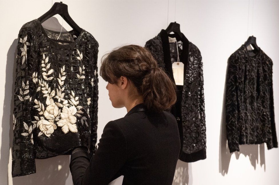 A woman examines a black and white appliqué jumper on show before the sale