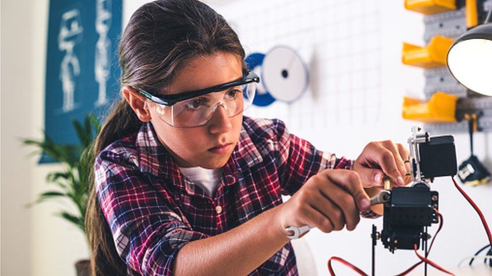 Girl in a robotics laboratory adjusts the robot arm model