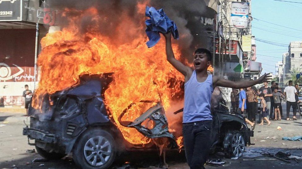 Палестинский мальчик реагирует перед горящей израильской машиной в секторе Газа (10.07.23)