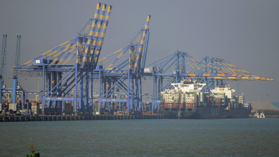 Cargo ship at the port of Mundra, next to several large metal cranes.