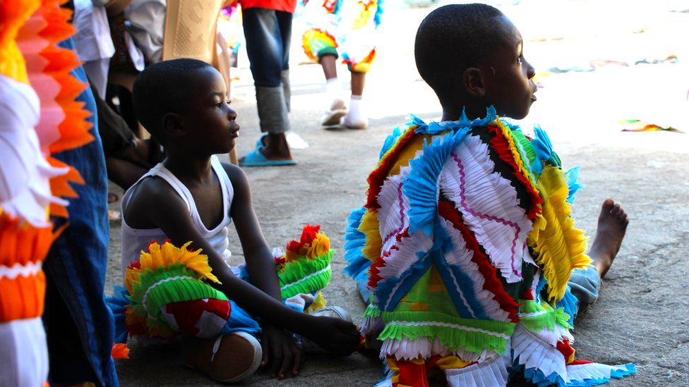 Children sit in multi-coloured outfits, made up of faux-feathers in Sekondi Ghana