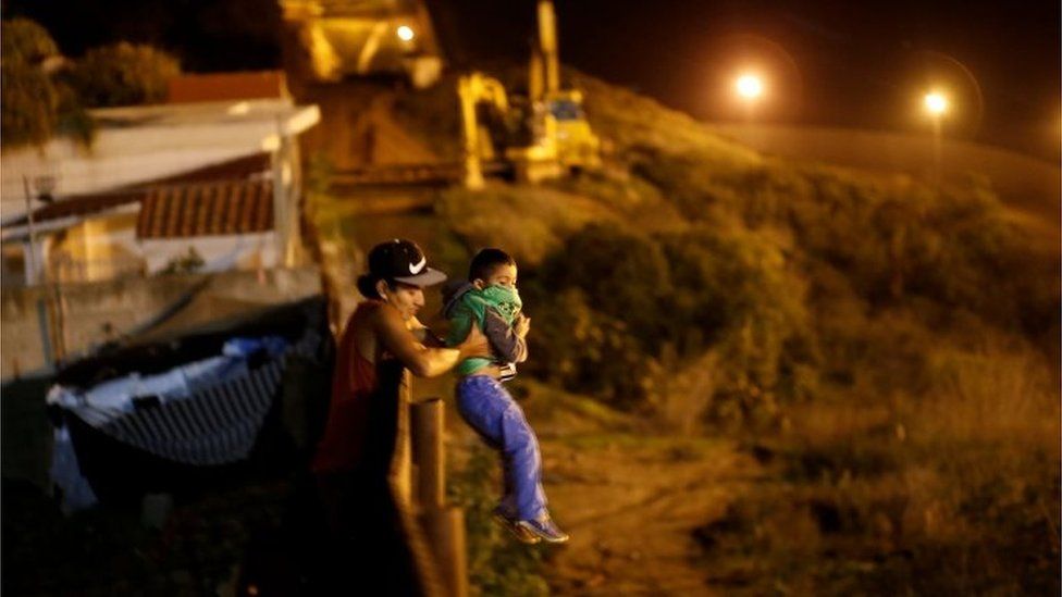 A migrant from Honduras helps a child to jumps the fence to cross it illegally from Mexico into the U.S., in Tijuana, Mexico, January 13, 2019.