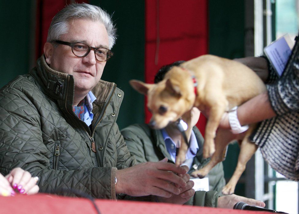 Prince Laurent of Belgium is presented with a small dog while judging a dog show in 2014