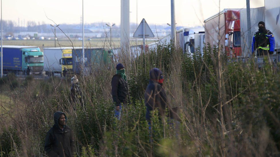 Migrants on a roadside embankment beside a line of lorries near Calais