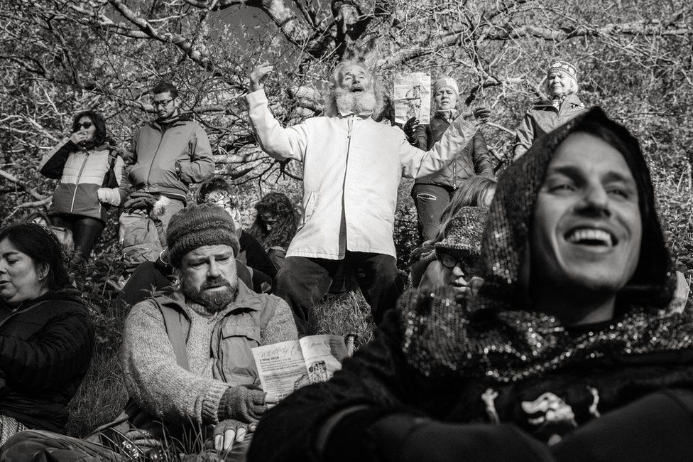 A man sings in a field whilst surrounded by people