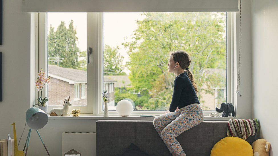 Young girl looking out of her bedroom window.