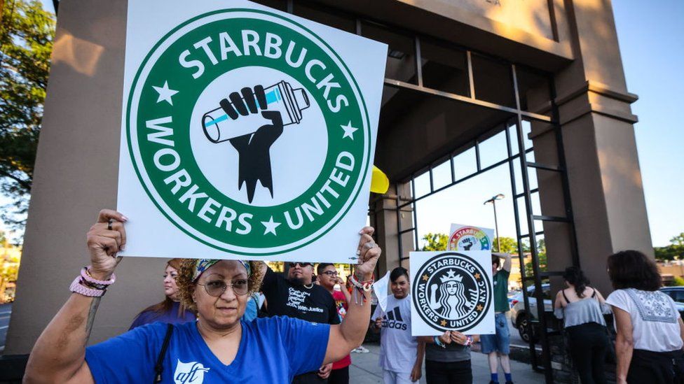 Great Neck, N.Y.: A woman holds up a sign as she joins other protestors in a rally against what they perceive to be union busting tactics, outside a Starbucks in Great Neck, New York, demanding the reinstatement of a former employee on August 15, 2022.