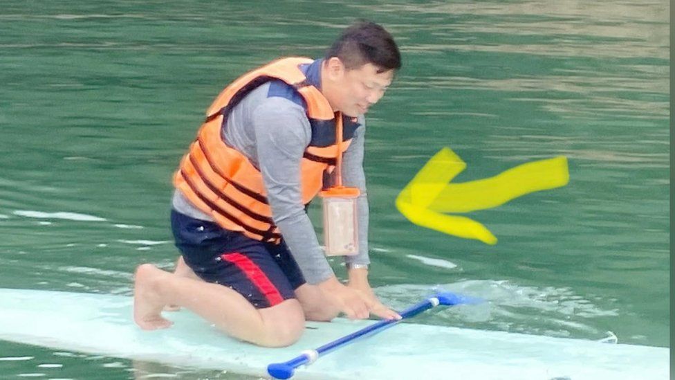 Mr Chen paddleboarding with his phone hung on a lanyard
