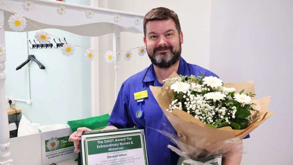 Stewart Hilton pictured in his scrubs holding an award and clutching a bouquet of flowers