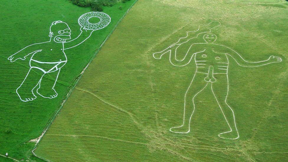 Homer Simpson painted with water-based biodegradable paint next to the 17th century giant which is carved in the hillside above Cerne Abbas,
