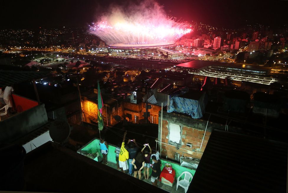 Personas en el patio de una casa en un favela viendo desde lo alto los fuegos artificiales en el Estadio Maracaná