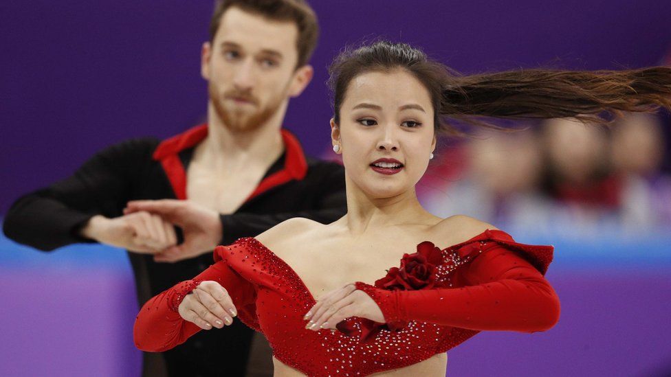 Yura Min puts on a brave face as she suffers a wardrobe malfunction during her routine as her skating partner Alexander Gamelin looks on