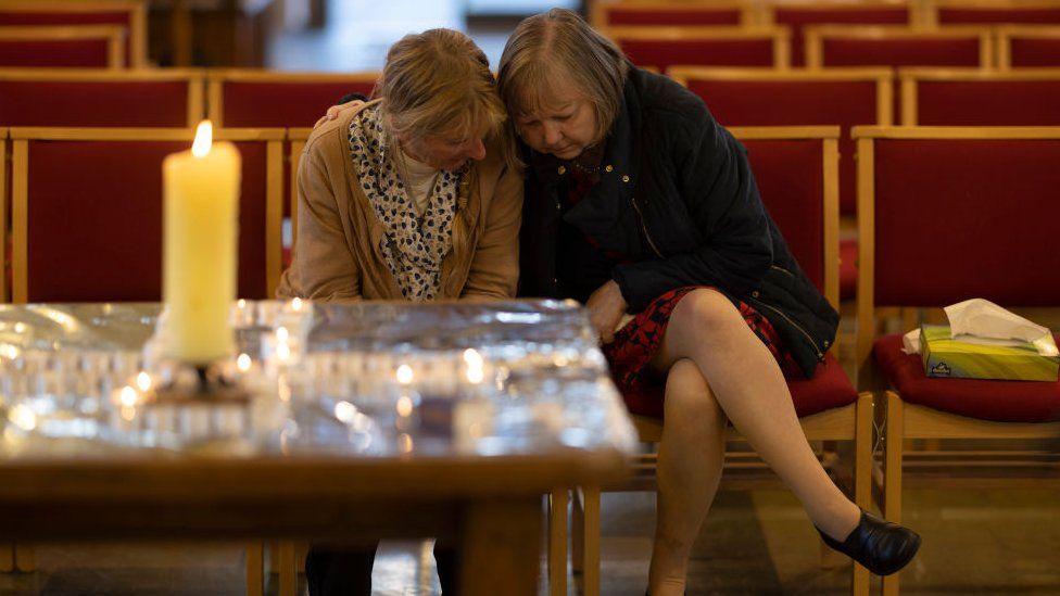 Two women gather their thoughts at a church before lighting a candle for Sir David Amess