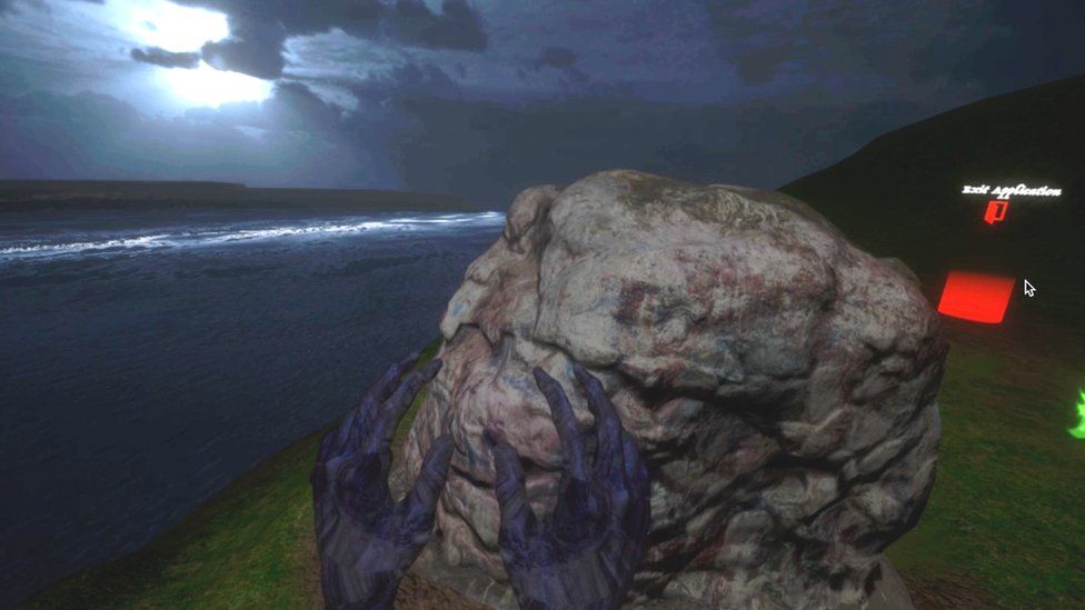 A screengrab from the virtual reality project shows two hands reaching towards a large rock by the sea on a moonlit light