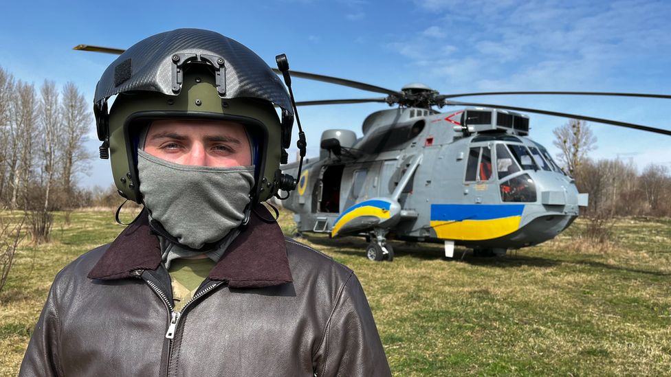 Ukrainian pilot Vasil, pictured with his face covered in front of a Sea King helicopter donated by the UK and painted with the blue and yellow stripes of the Ukrainian flag.