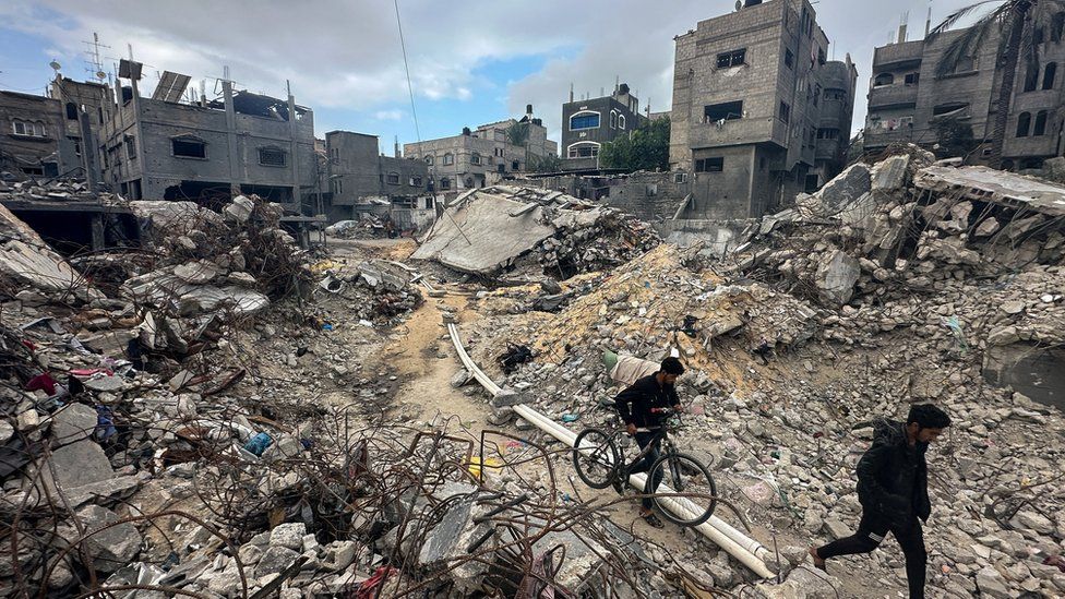 Palestinians walk through rubble in Khan Younis refugee camp, in the south of the Gaza Strip (27 November 2023)