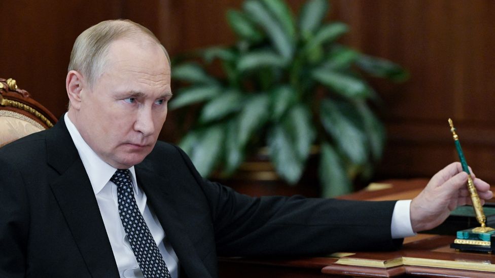 Vladimir Putin sits at a desk