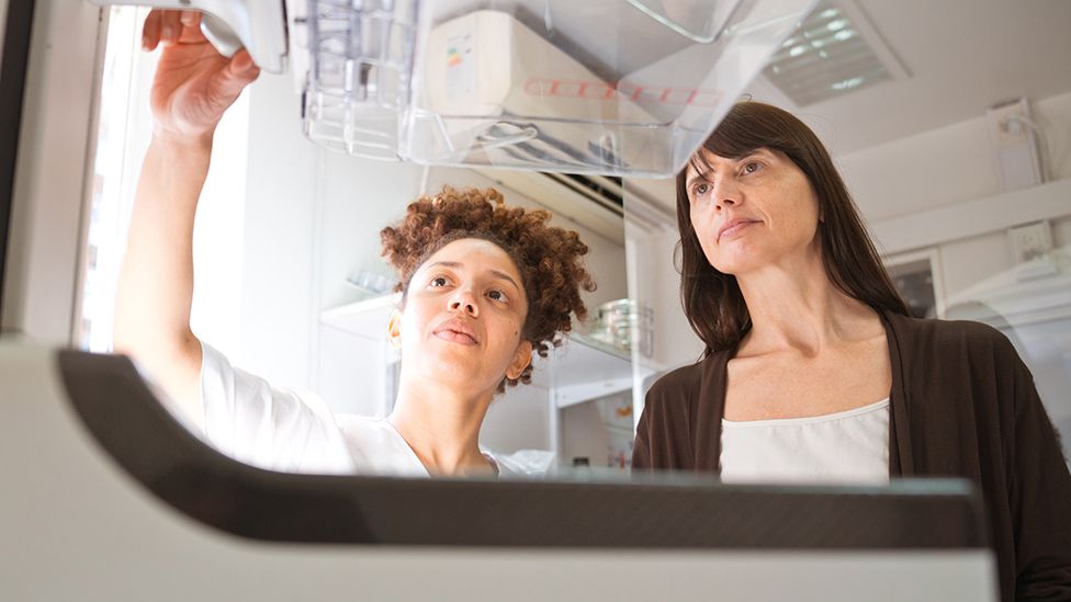 A healthcare professional and a patient discuss mammography results as they stand behind a scanner