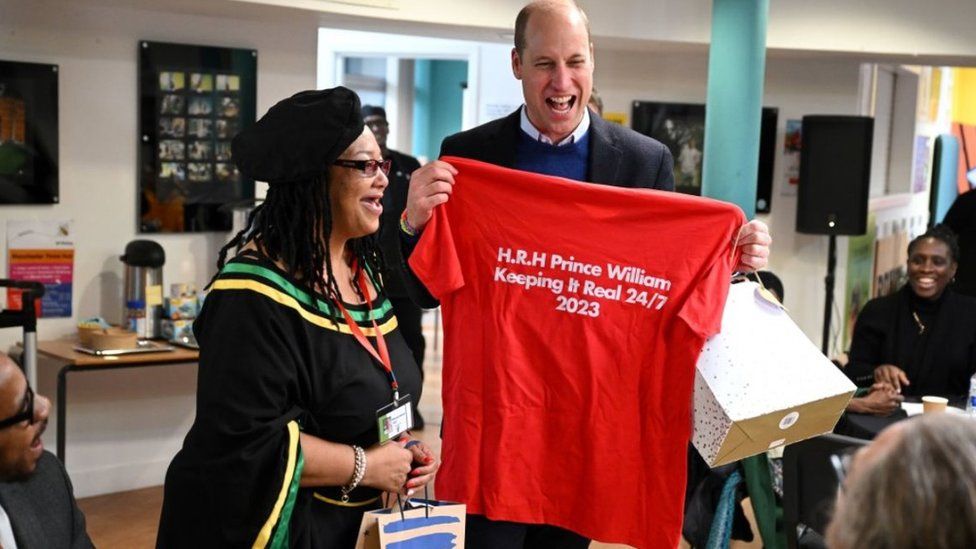 The Prince of Wales receives a t-shirt during his visit to the Moss Side Millennium Powerhouse, a community hub