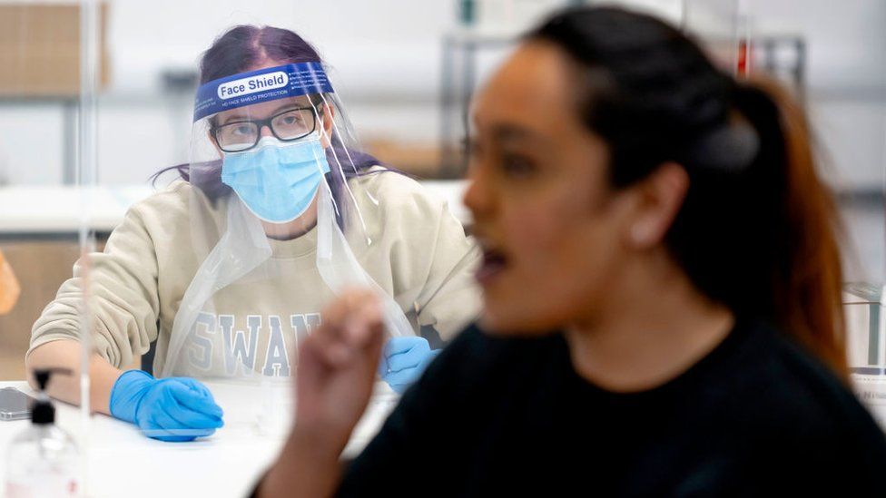 A medical staff looks on as a student inserts a swab into her mouth as part of a COVID-19 lateral flow test at Swansea University on December 8, 2020 in Swansea, Wales.