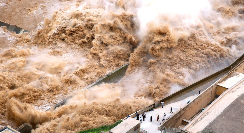 Water from a dam rushes past people
