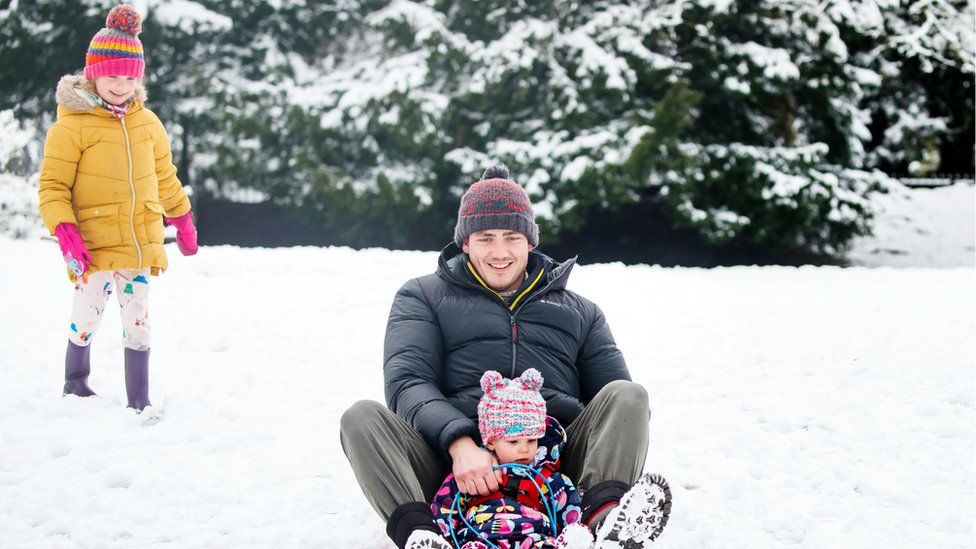 Dan Ives with his daughters Eden (on the sledge) and Poppy (left) in a snow covered Buxton Park in Buxton, Derbyshire